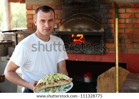 Pizza chef holding plate with freshly baked pizza at an outdoors restaurant.