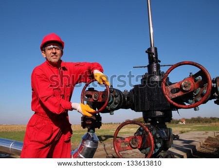 Oil and Gas Worker Wearing Protective Clothing. Smiling oil worker turning valve on oil rig. Oil pump jack in a field.