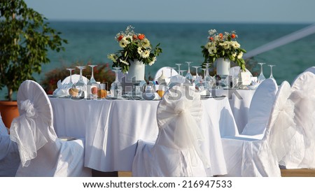 Outdoor Table Setting at Wedding Reception by the Sea. Wedding Chairs and covers at an outdoor wedding. Elegant Outdoor Wedding Table with Sea Views. Table set for an event party or wedding reception.