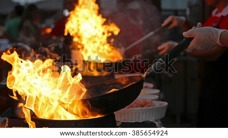 Flambe Chef Cooking in Outdoor Kitchen. Professional chef in a commercial kitchen cooking flambe style. Chef Flambe Cooking.