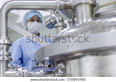 Portrait of Pharmaceutical Worker. Preparing machine for work in pharmaceutical factory. Female worker wearing protective clothing in pharmaceutical plant.\
Biomedical and pharmaceutical research.