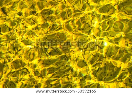 Yellow and brown water surface reflections making shadows on a rocky river bed