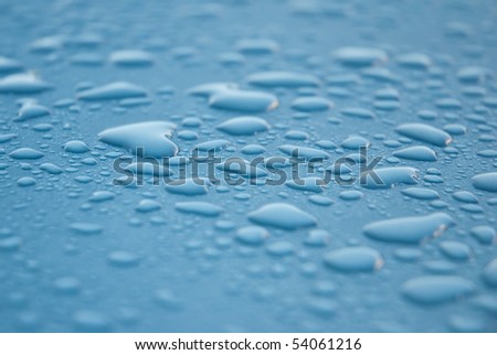 Close-up shot of dew drops on a light blue or turquoise metallic surface, glistening from the light