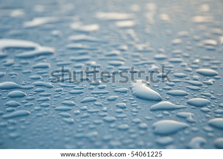 Close-up shot of dew drops on a light blue or turquoise metallic surface, glistening from the light