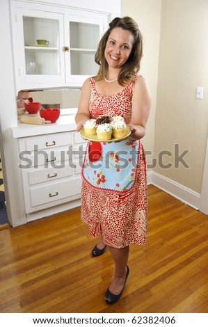 An attractive woman in vintage clothing offers cupcakes to her guests.