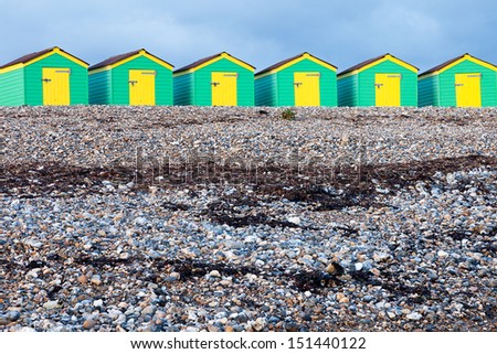 A row of green and yellow beach huts on a cloudy day.  Taken on the South Coast of England.
