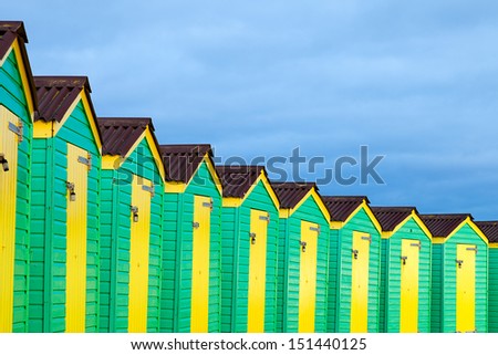 A row of green and yellow beach huts on a cloudy day.  Taken on the South Coast of England.