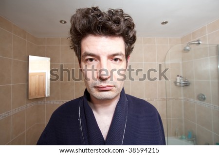 A man who has just woken up looks into the bathroom mirror.