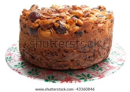 An isolated fruit cake topped with nuts and glace cherries on a christmas themed base.