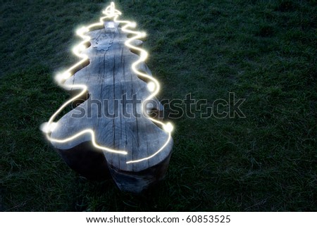 A wooden bench surrounded by grass at night.  An LED light has been used to trace the outline of the bench to make it look like a Christmas Tree.