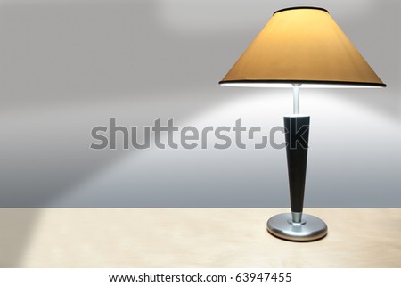 A simple lamp with yellow shade on a wooden desk casting a shadow onto a plain wall.