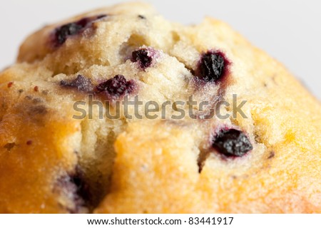 An extreme closeup of the top of a blueberry muffin on a white background.  Shallow depth of field with the focus on the centre blueberries.