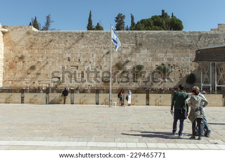 Jerusalem, Israel - November 9, 2014 : Tourists at Jerusalem\'s wailing wall compound with blue sky, the Israeli flag and the wailing wall in the background