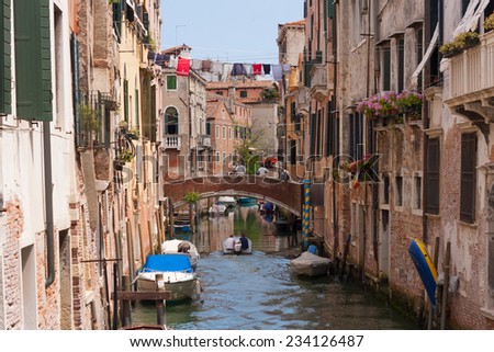 Venice, Italy - June 21, 2014: Typical view of a narrow canal with boat, bridge and old houses of Venice, Italy. With people.