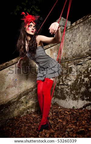 Beautiful girl wearing red hat and striped dress posing as a marionette (puppet on a string)