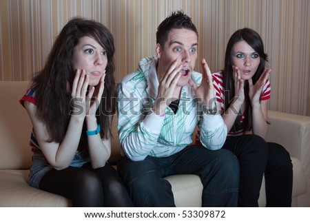 Three friends sitting on the couch in the living room and watching something scary on TV