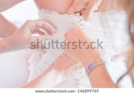 As the bride prepares for her wedding day, the maids button and lace up the back of her gown