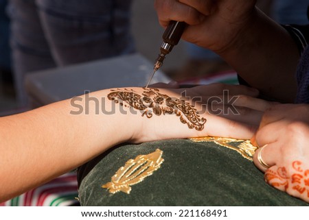 Image detail of henna being applied to hand over green and gold fabric cushion