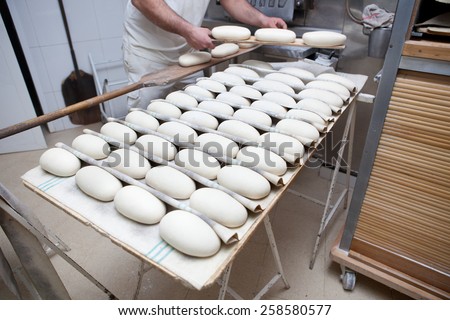 Baker putting bread dough into the oven. Selective focus. Manufacturing process of spanish bread