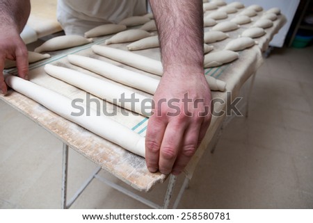 Male baker kneading and placing pieces of bread over fermentation sheet. Manufacturing process of spanish bread
