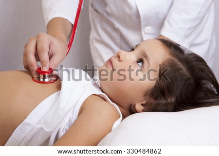 Pediatrician in white lab coat examines little girl