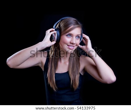 Young woman listening to music with headphones on black background.