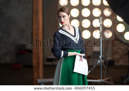 Portrait of a serious young woman standing backstage with her scripts wearing black sweater and green skirt