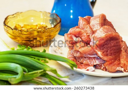 Raw meat,leek, blue pitcher and gold bowl on white kitchen board