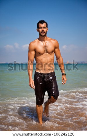 Handsome muscular man walking out of the water on a turquoise water beach.