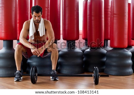 Handsome muscular sports man with a towel on his shoulders looking tense in front of red punching bags. Fighter.
