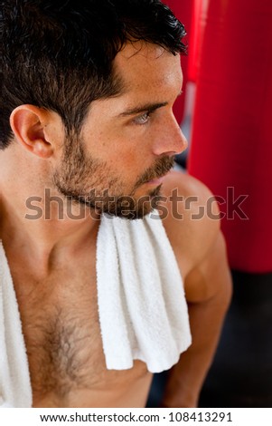 Handsome muscular sports man with a towel on his shoulders looking tense in front of red punching bags. Fighter.
