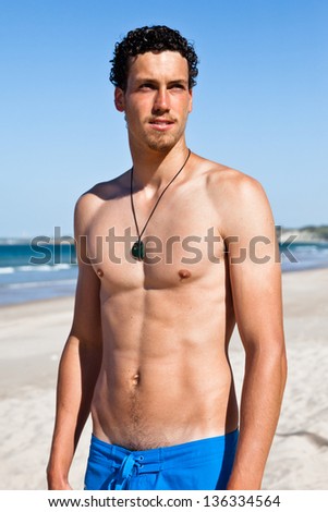 Young handsome muscular man in a bathing suit hanging on the beach. Surfer type.