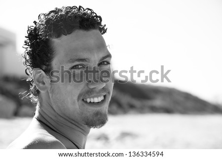 Close up portrait of a cute young man with a goatee smiling on the beach. Black and white.