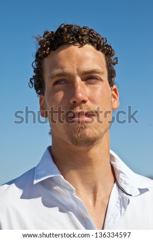 Close up portrait of a young handsome man with a goatee, a tan and wet curly hair wearing a white shirt. Mediterranean type.