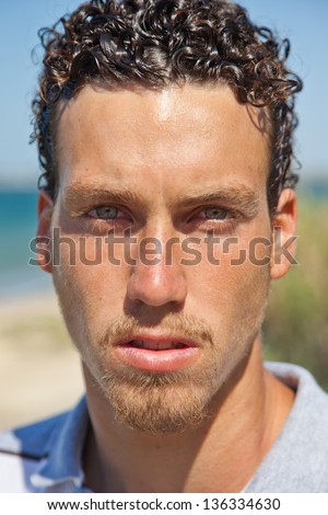 Close up portrait of a young handsome man with a tan and wet curly hair. Mediterranean type.