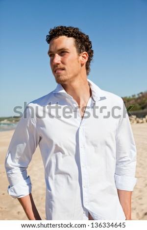 Young handsome man with a tan and wet curly hair wearing a white shirt hanging at the beach. Mediterranean type.