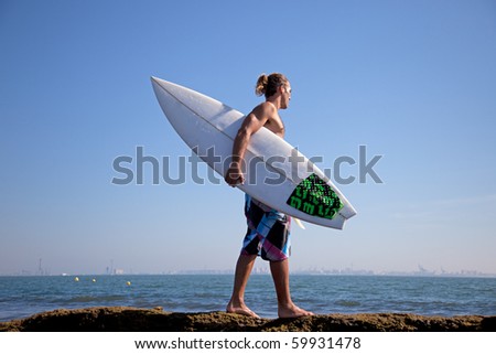 Surfer holding his board walking on rocks with ocean behind him