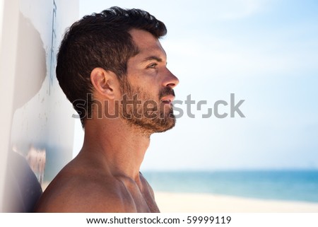 Handsome surfer looking at the sea with his board behind him. Side view