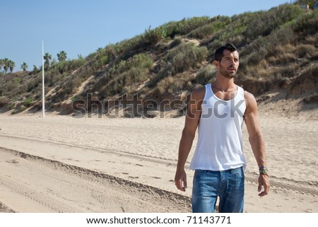 Young handsome man on the beach looking worried, dressed in casual clothes: plain white shirt and jeans.