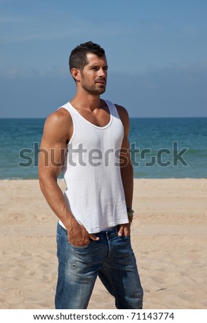 Young handsome man on the beach looking worried, dressed in casual clothes: plain white shirt and jeans.