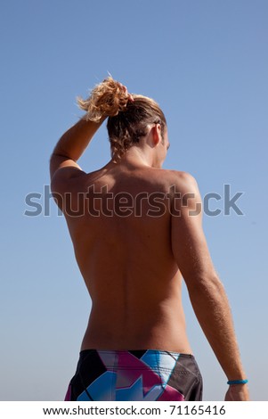 Back of a fit blonde male surfer fixing his hair.