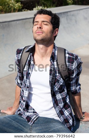 Handsome college student with backpack sitting down enjoying the sun in a spring day.