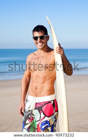Handsome muscular surfer wearing sunglasses smiling at camera holding his surf board.