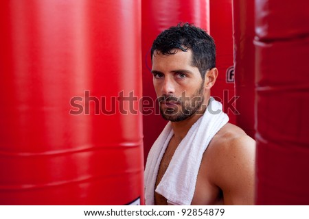 Attractive muscular man with a towel on his shoulders looking worried and angry in between red punching bags. Fighter.