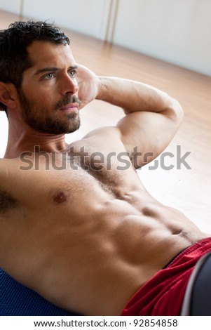Handsome muscular man doing sit-ups on a wooden floor.