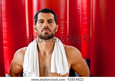 Handsome muscular sports man sweating with a towel on his shoulders looking at camera in front of red punching bags. Fighter.