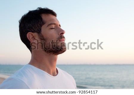Handsome man wearing white deep breathing in front of the ocean.
