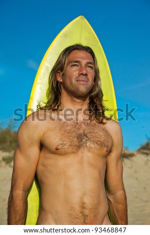 Attractive long haired blonde surfer standing in front of his surfboard.