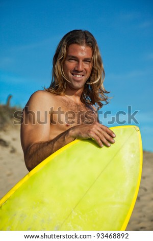 Long haired blonde surfer holding his surfboard in front of him.