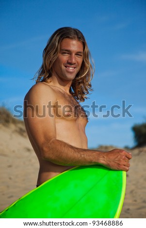 Long haired blonde surfer holding his surfboard in front of him.